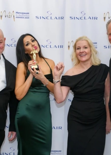 Group at an awards evening, one woman holding a gold trophy, in front of a sponsor backdrop