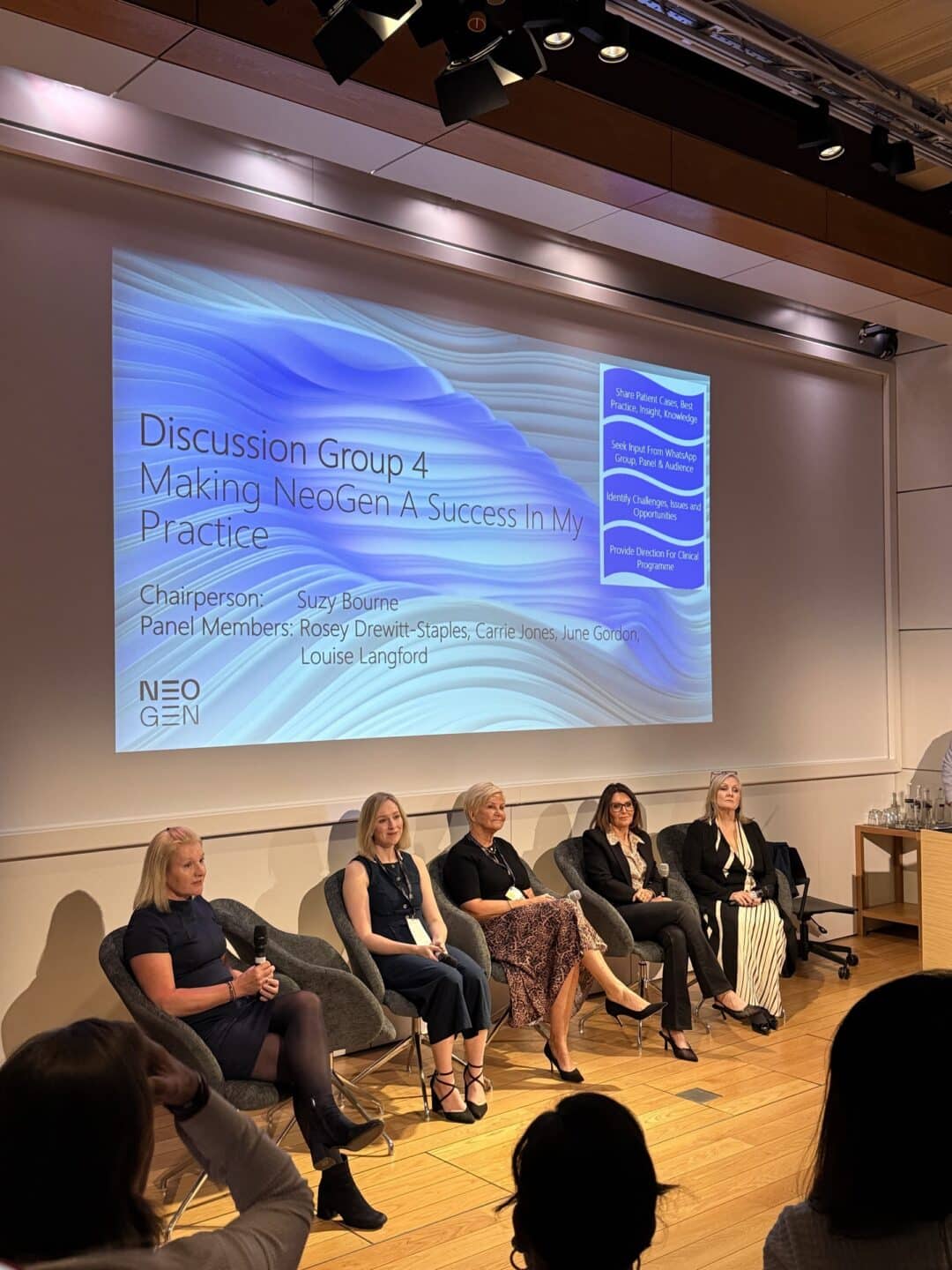 A panel of practitioners on stage under a NeoGen slide at the NeoGen Global Summit in London