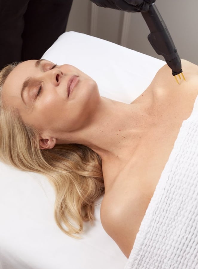 Woman with blonde hair lying on a treatment couch as a NeoGen handpiece is held near her neck