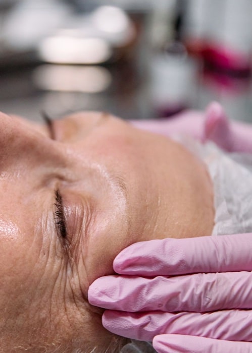 Close-up of the lined skin around a woman’s eye, with a pink-gloved hand beside it
