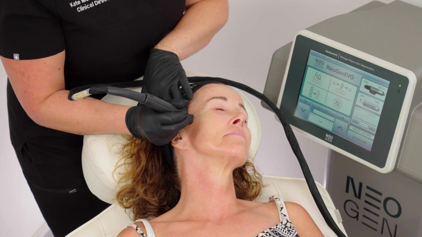 Practitioner treating a patient’s temple with the NeoGen EVO handpiece, the device screen beside them